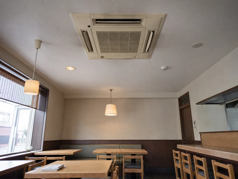 飲食店の無人の客席の上に取り付けられた天井カセット形エアコン（イメージ写真）